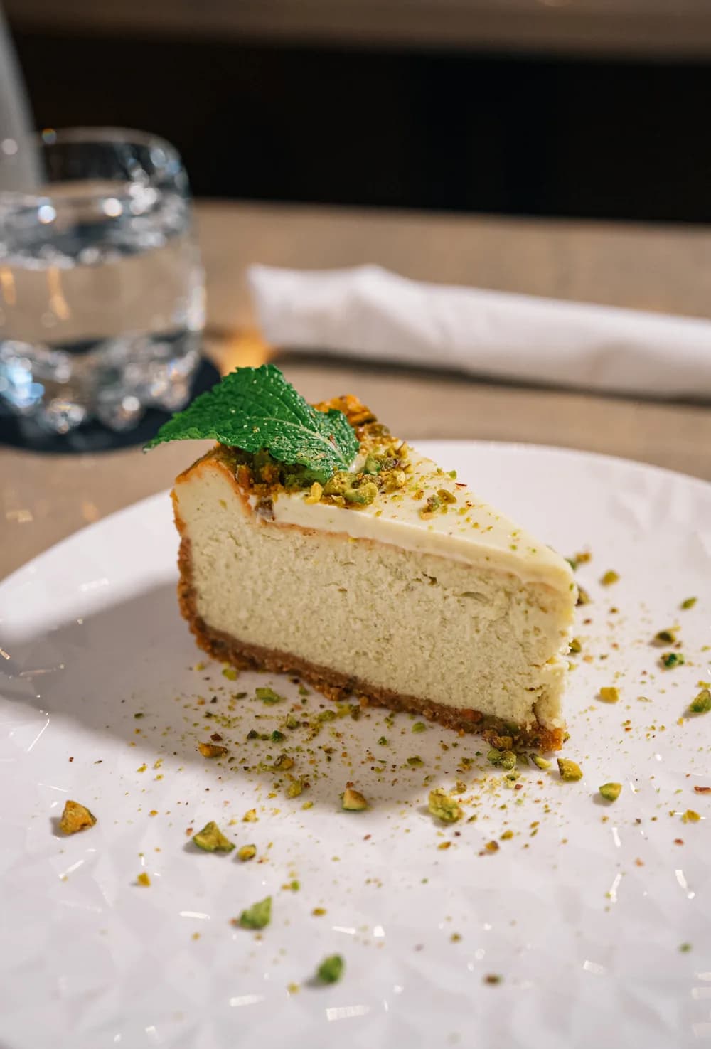 A slice of pistachio cheesecake topped with fresh mint on a white plate.